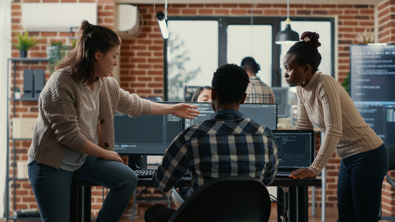 A team if office workers gathered around a workspace discussing something on a computer screen