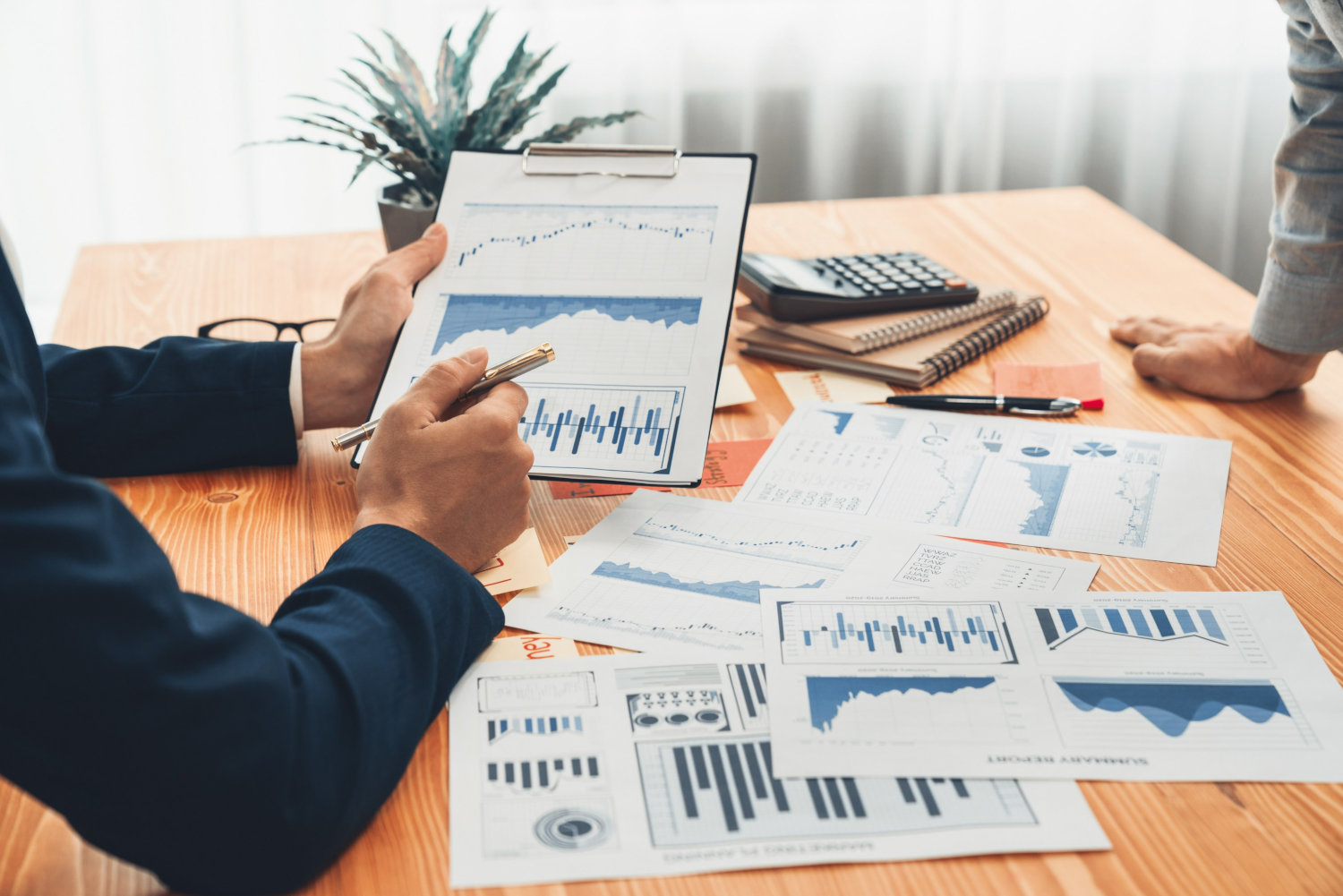 People discussing charts on a tablet with various other charts on paper strewn around a desk